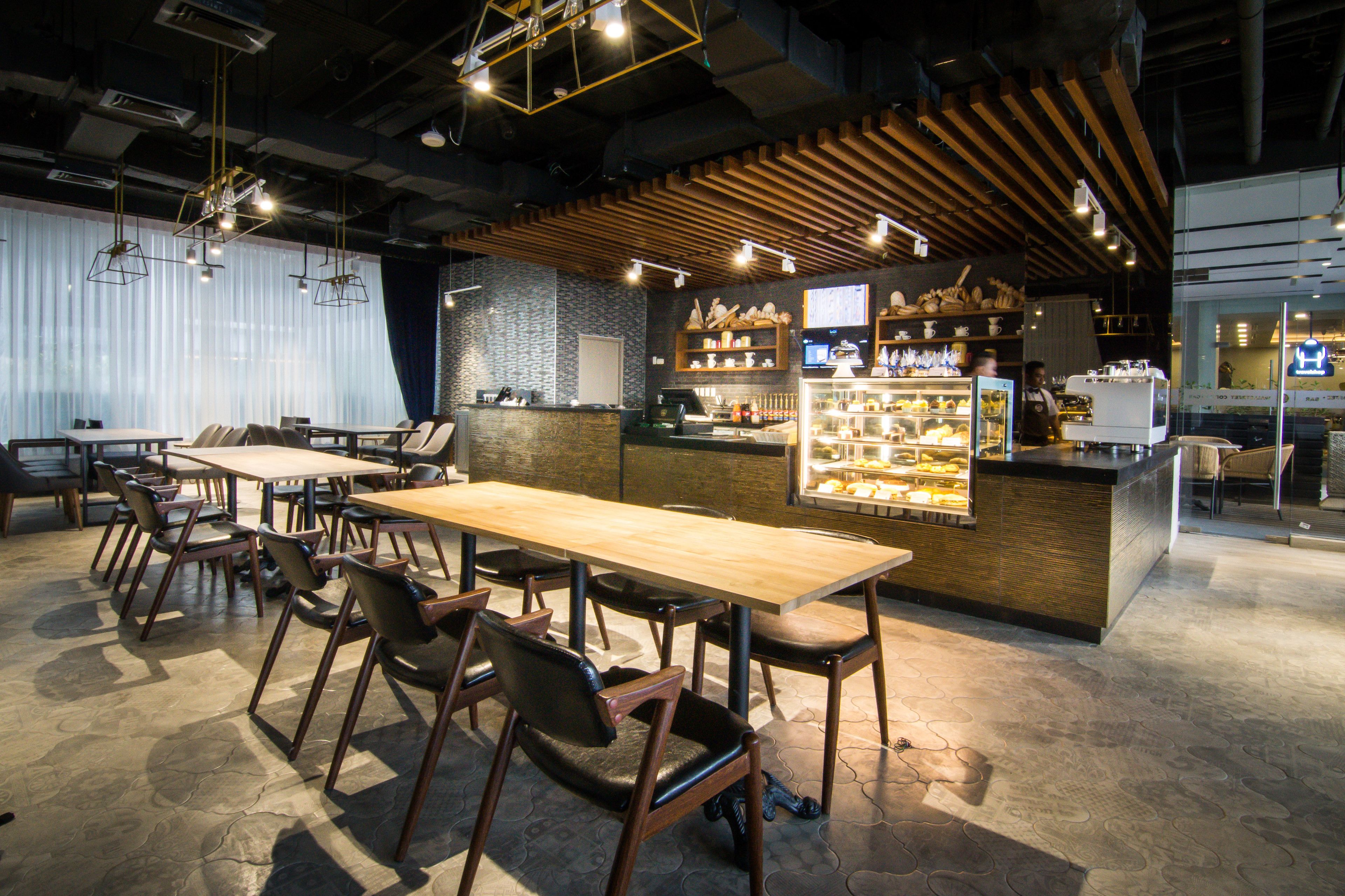 A restaurant with wooden tables and chairs, a counter with a display case, and hanging lights.