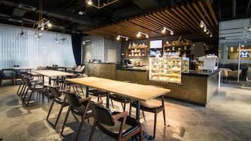 A restaurant with wooden tables and chairs, a counter with a display case, and hanging lights.
