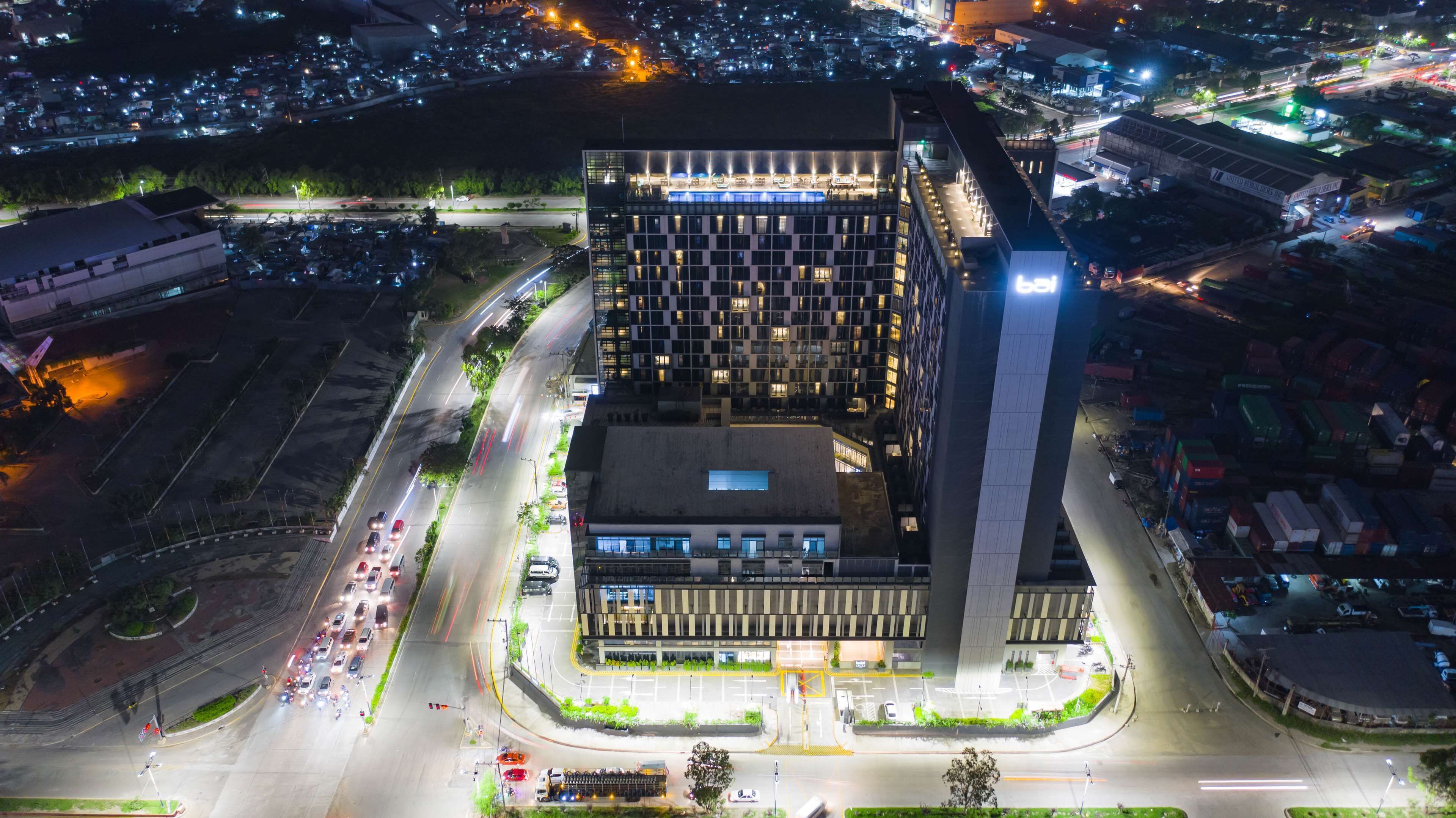 Vista aerea di un edificio moderno con una struttura verticale ben definita, circondato da strade e altri edifici.