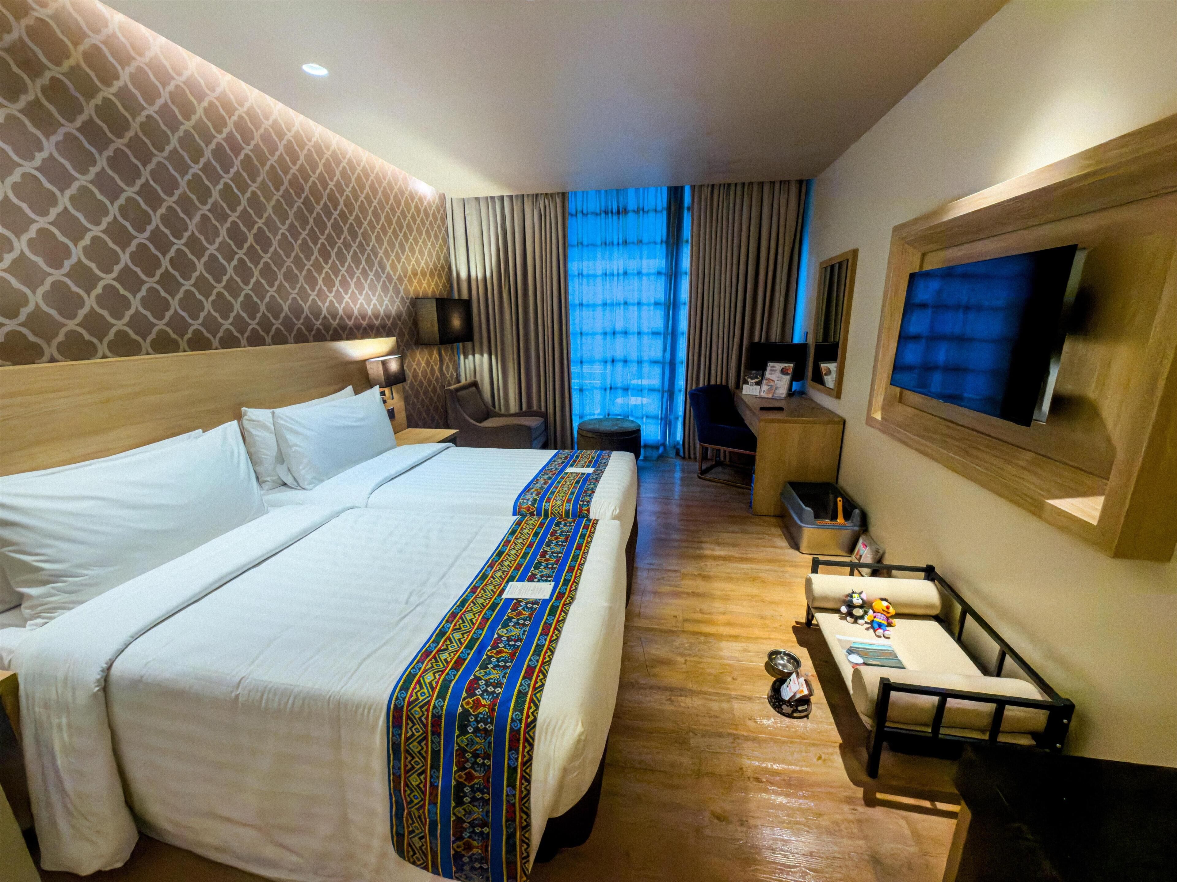 Habitación de hotel con una cama grande, un escritorio con silla, un televisor y una ventana con cortinas.