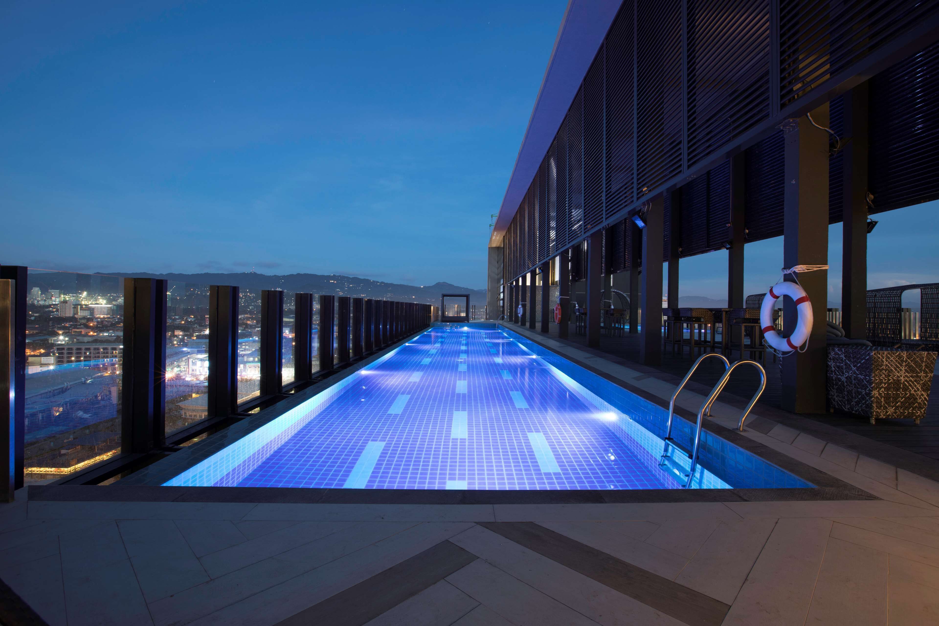 Une piscine à débordement située sur le toit, offrant une vue sur la ville, avec une bouée de sauvetage et une échelle métallique.