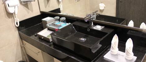 Un baño moderno con un lavamanos negro, un espejo, un secador de pelo y un cubo de basura.
