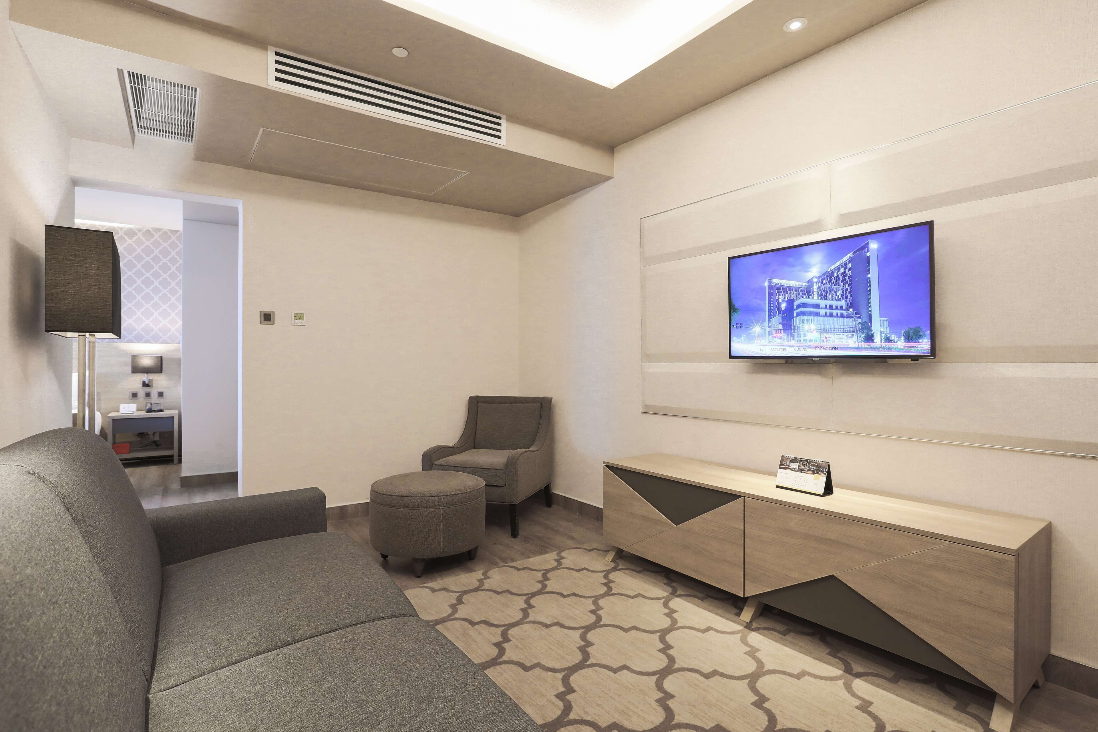 A modern living room with a sofa, ottoman, and a TV mounted on the wall.