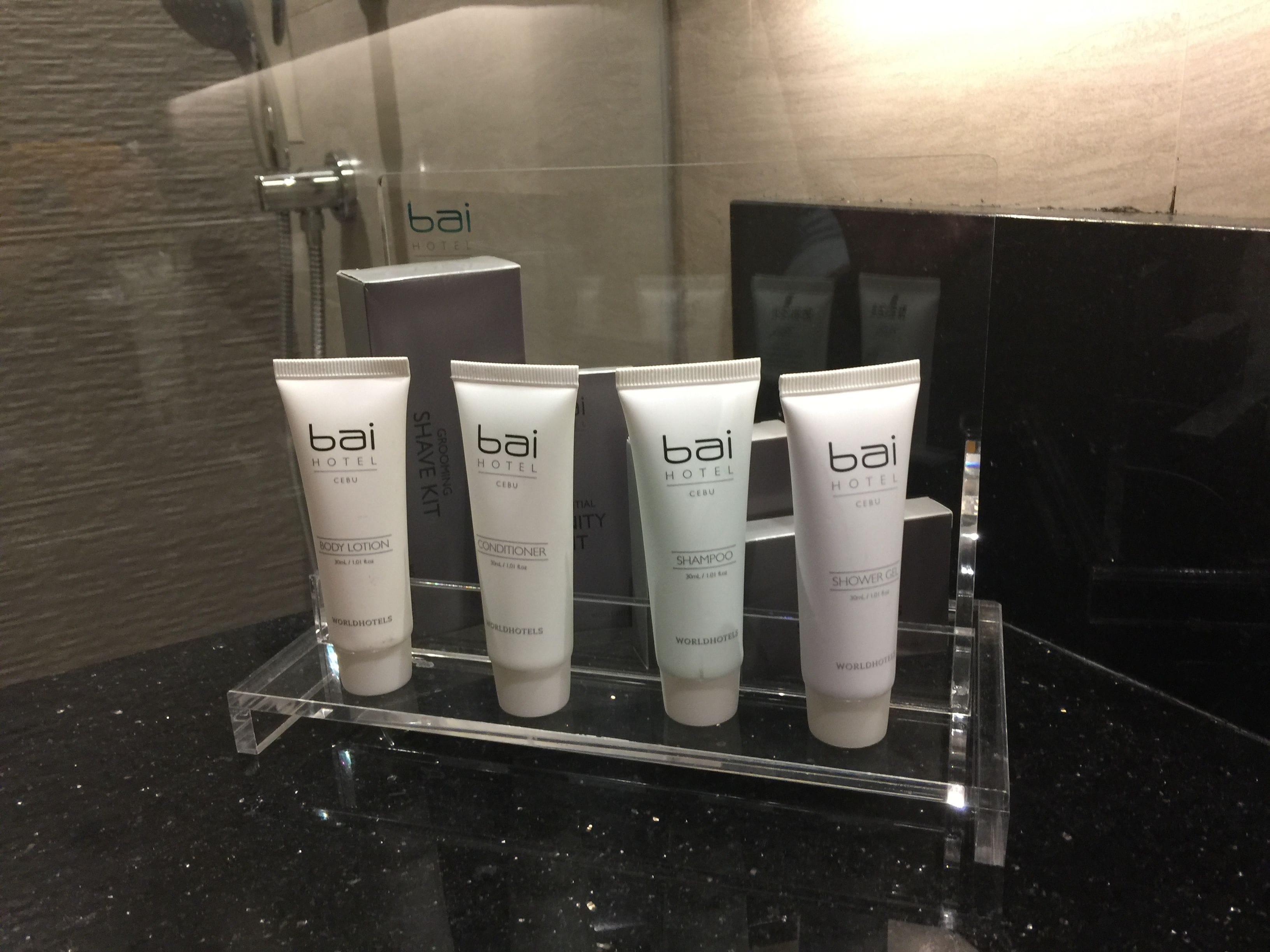 A bathroom display with four bottles of Bai Hotel Cebu body lotion, conditioner, shampoo, and shower gel.