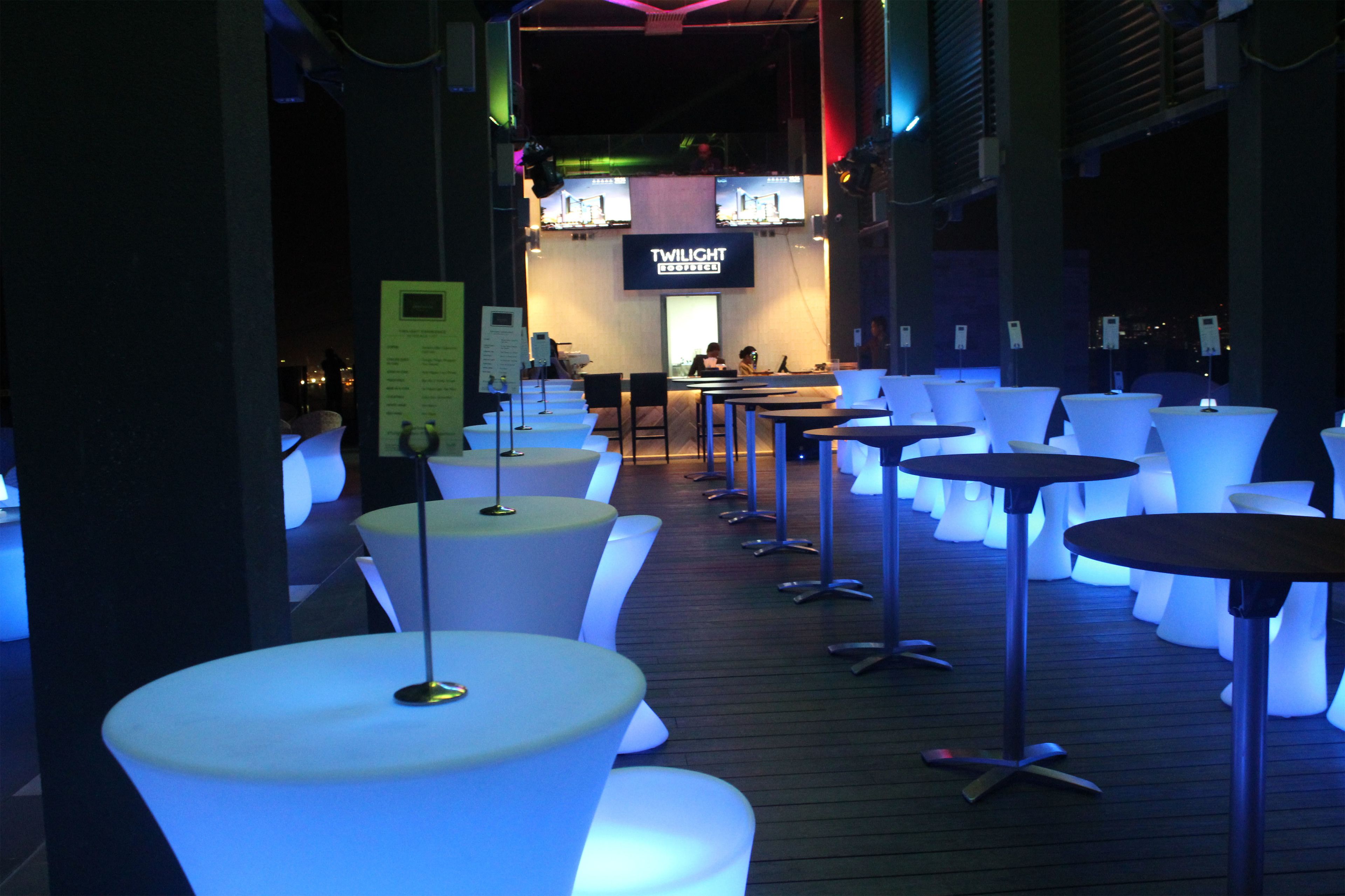 Eine moderne Bar mit beleuchteten weißen Tischen und einem Schild mit der Aufschrift 'Twilight Lounge'.