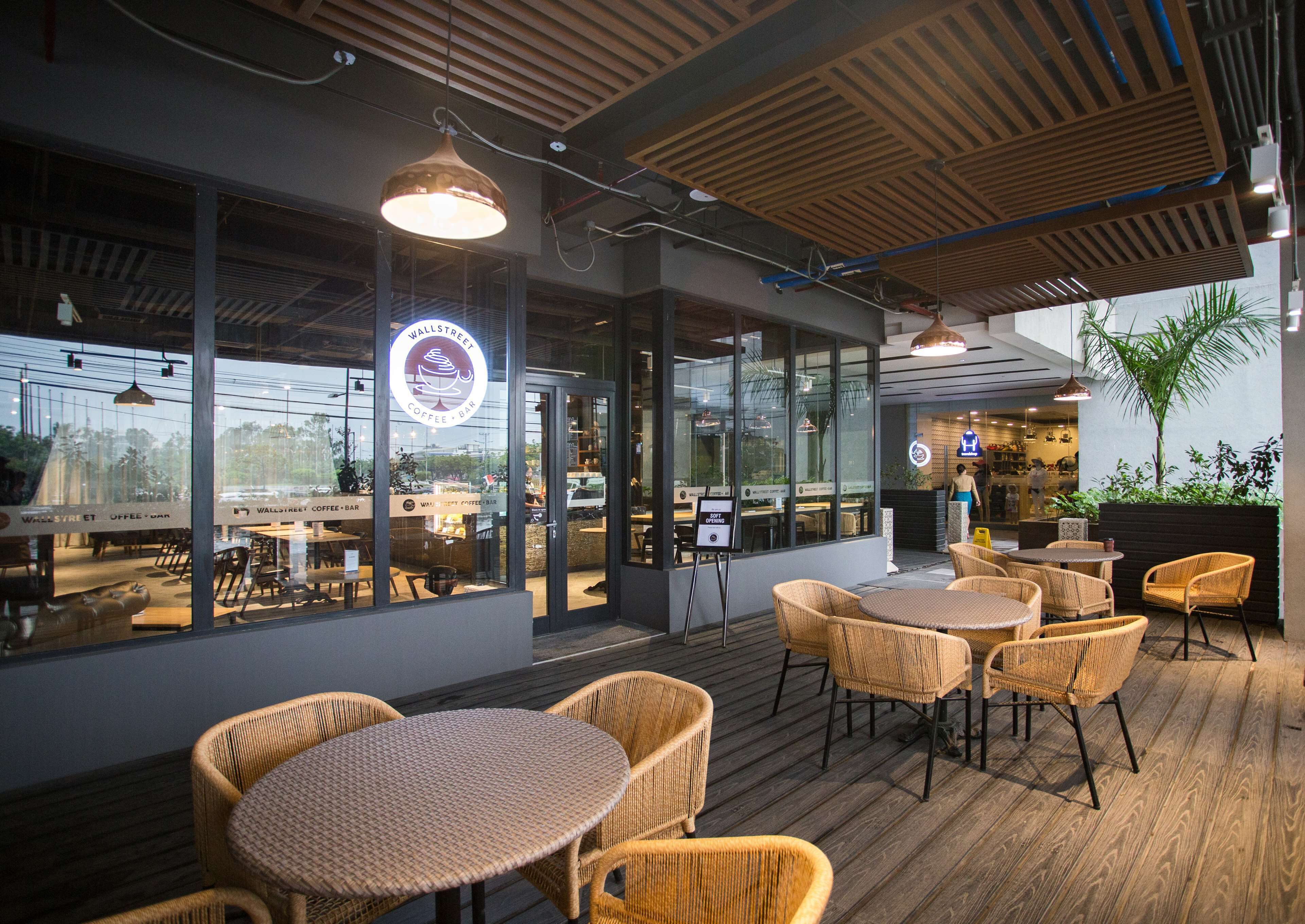 An outdoor seating area with wicker chairs and tables, a coffee bar sign, and large windows.