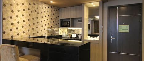 Une cuisine moderne avec un îlot central en marbre noir, un four à micro-ondes et une machine à café. On y trouve une porte avec une pancarte et une chaise dans un coin.