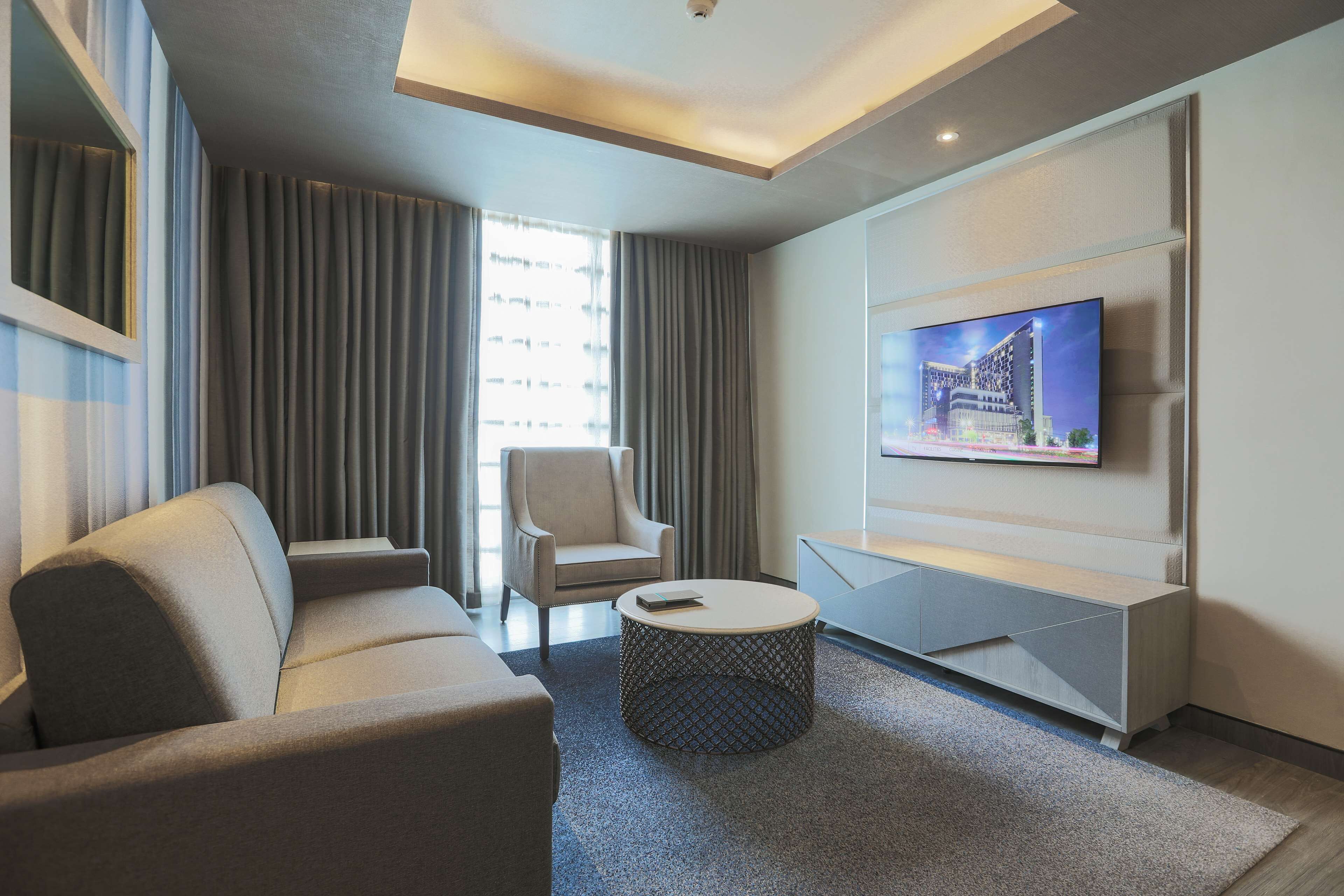 A modern living room with a sofa, armchair, coffee table, and a TV mounted on the wall.