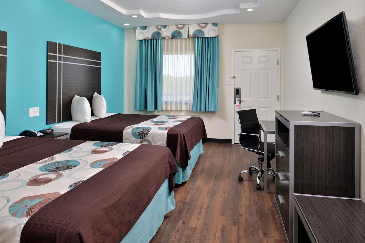 A hotel room with two beds, a desk, a chair, a TV, and a door.