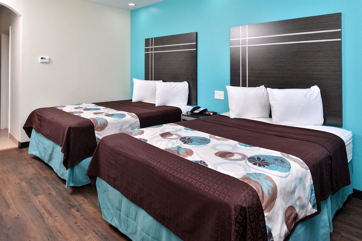 A hotel room with two beds, each with a patterned bedspread and pillows, a wooden floor, and a blue accent wall.