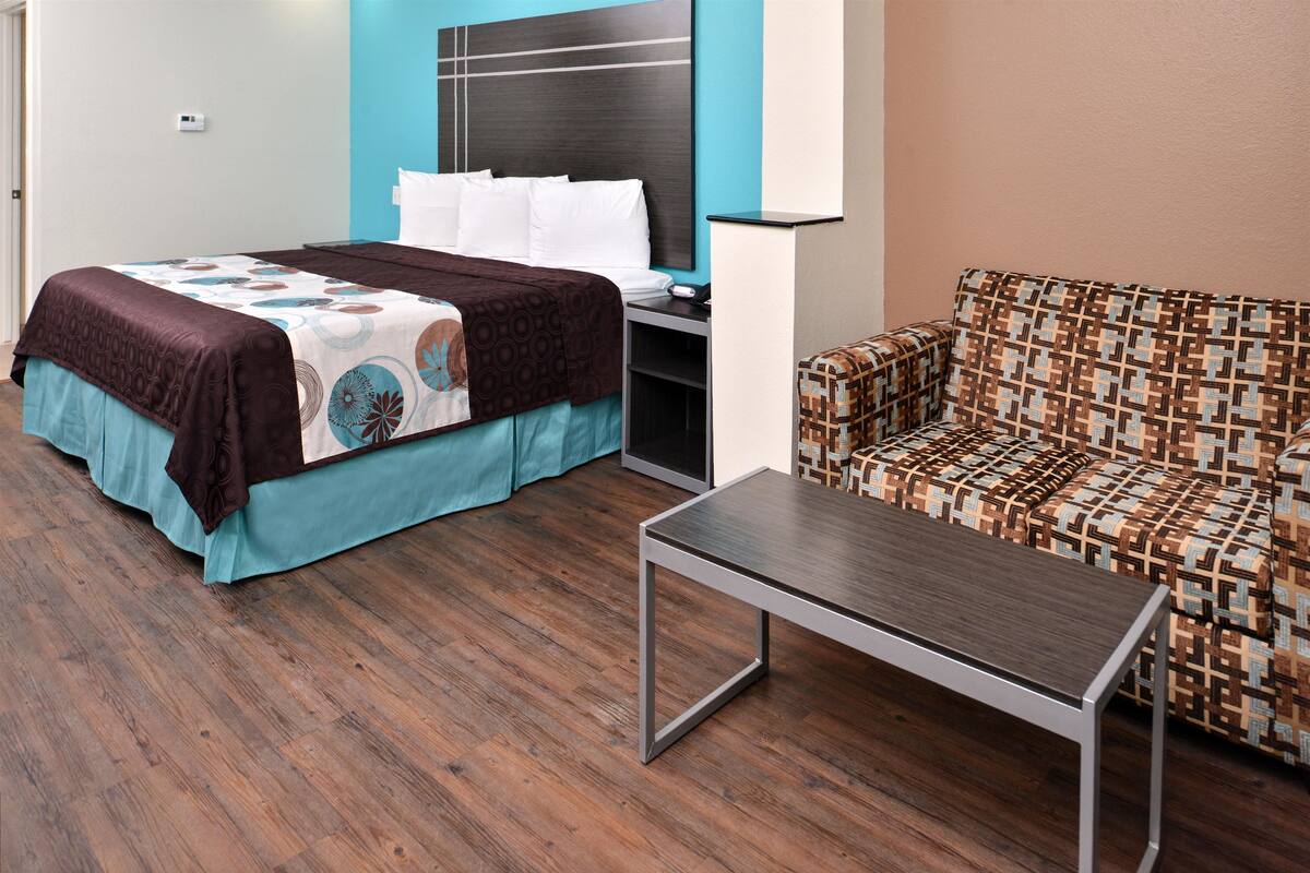 A hotel room with a bed, a sofa, a small table, and a wall-mounted lamp.