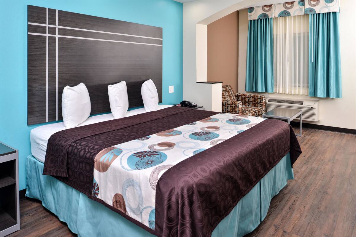 A modern hotel room with a large bed, a bedside table, a chair, and a window with curtains.