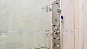A glass-enclosed shower with a control panel, marble walls, and a towel rack. - Americas Best Value Inn & Suites Spring Houston N (Spring)