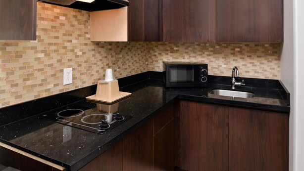 A kitchen with dark wooden cabinets, a black countertop, a microwave, and a sink. - Americas Best Value Inn & Suites Spring Houston N (Spring)