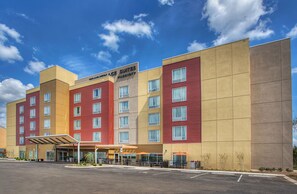 A multi-story hotel with a modern facade, featuring a mix of red and beige colors, and a covered entrance area with outdoor seating. - TownePlace Suites by Marriott Cookeville (Cookeville)