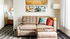 A modern hotel room with a sectional sofa, a small side table, and a floor lamp. - TownePlace Suites by Marriott Cookeville (Cookeville)