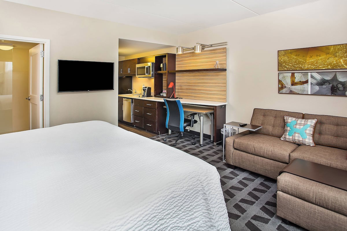 A hotel room with a large bed, a sofa, a desk with a chair, a flat-screen TV, a microwave, and a coffee maker.