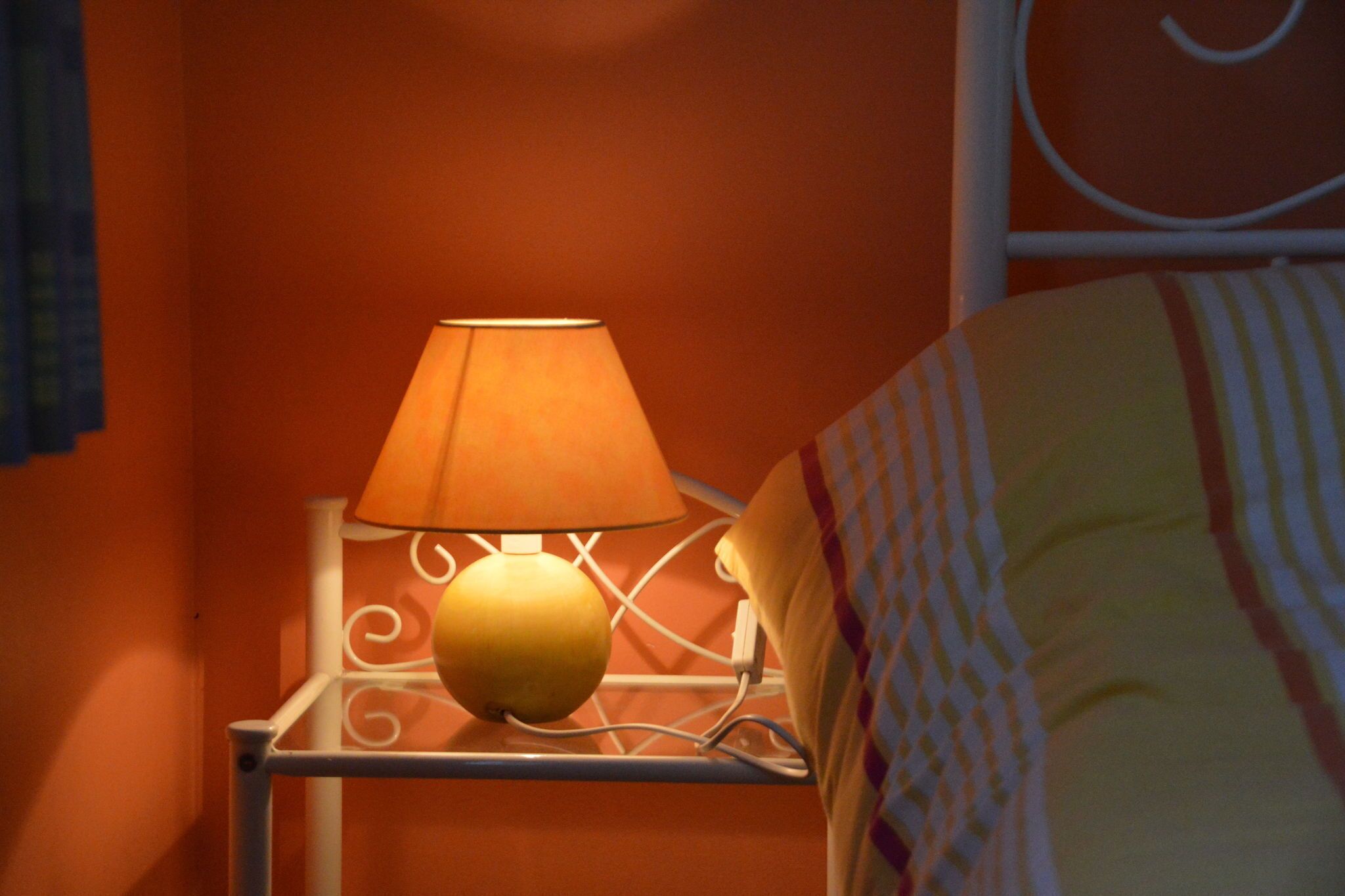 A lamp on a bedside table with a patterned bedspread.