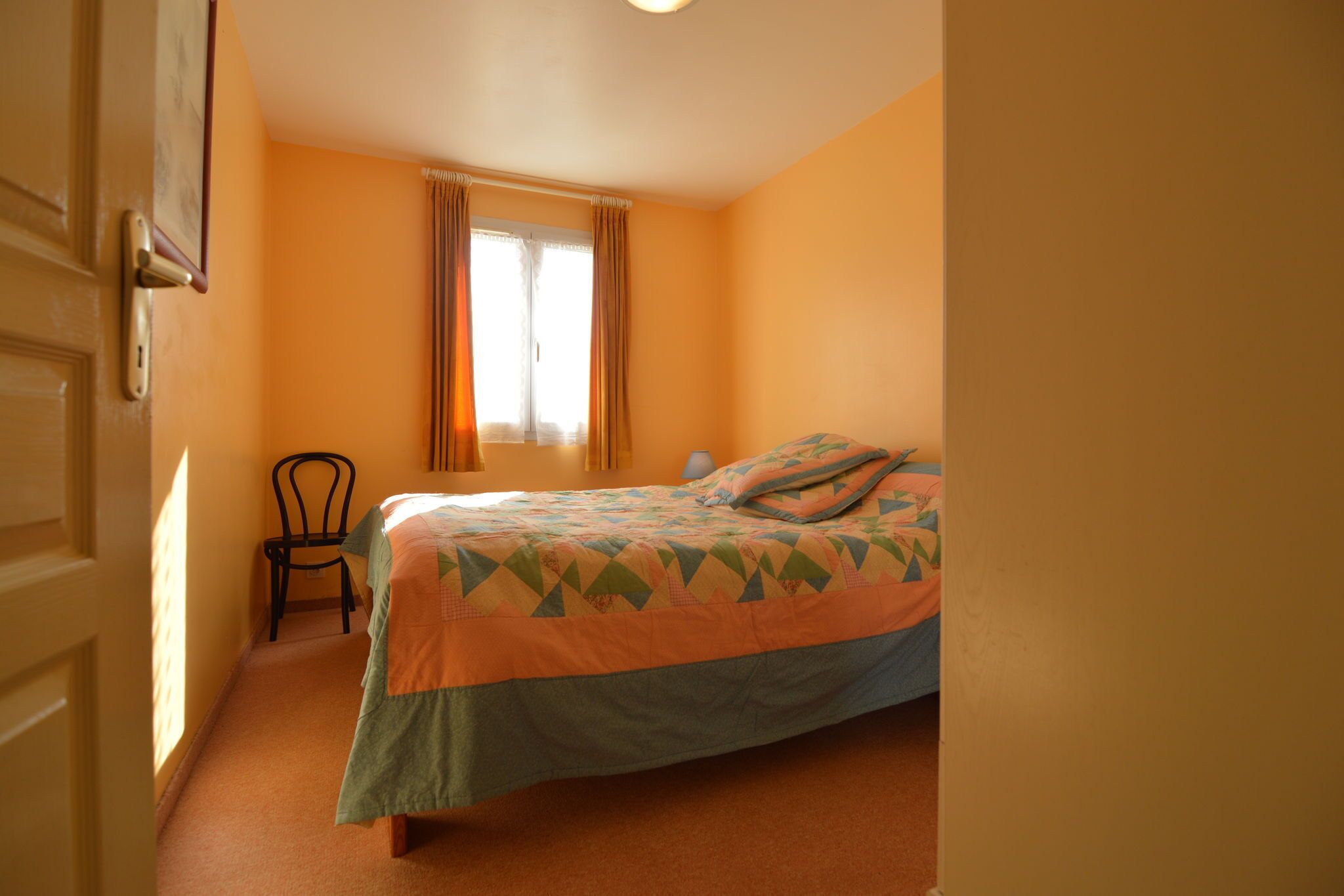 Ein Schlafzimmer mit Bett, Stuhl und einem Fenster mit Vorhängen.