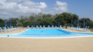 A swimming pool with blue chairs and umbrellas, surrounded by trees. - Quiet holiday home by the sea in the Loire (Talmont-St. Hilaire)