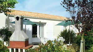 A house with a tiled roof, a front door, and a patio area with chairs and a table. - Quiet holiday home by the sea in the Loire (Talmont-St. Hilaire)