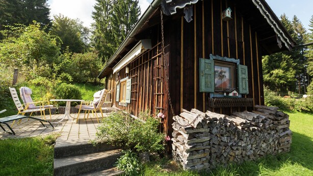 A wooden cabin with a stone foundation, a porch with chairs, and a small table.