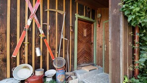 A rustic wooden building with a herringbone door, skis, a shovel, and various containers outside.