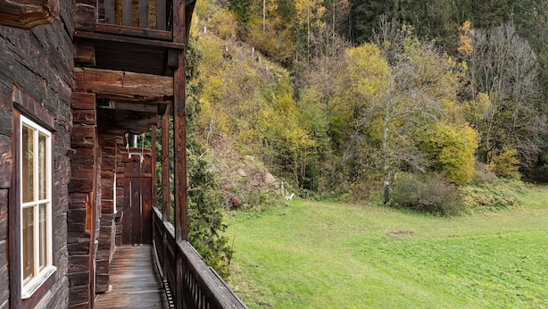 A rustic wooden cabin with a wooden deck and a grassy yard.