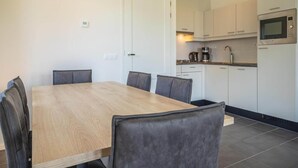 Moderni keittiö, jossa on valkoiset kaapit, mikroaaltouuni sekä ruokailutila, jossa on puinen pöytä ja tuolit.