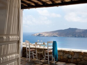 A seaside terrace with white chairs and a table, overlooking the sea and a distant mountain. - Villa in Mykonos near Agios Sostis Beach (Agios Sostis, Mykonos)
