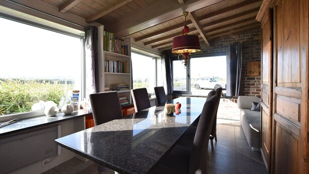Zona pranzo con tavolo in granito, sedie, lampadario rosso, libreria e vista sul verde attraverso ampie finestre.
