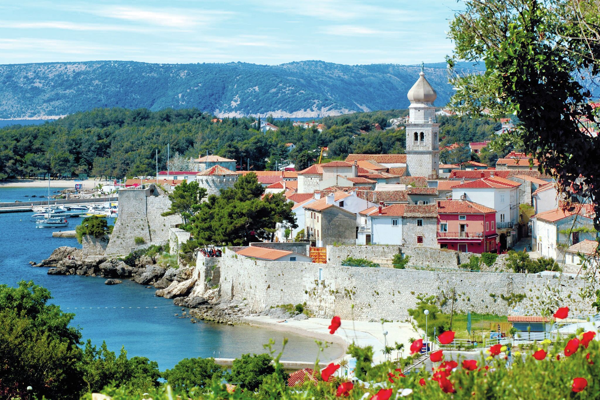 A coastal town with a prominent tower, stone walls, and red-roofed buildings.
