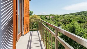 Un balcon donnant sur un paysage verdoyant et sur des bâtiments situés au loin.