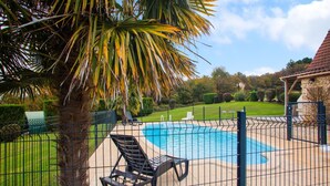 Ein Garten mit Swimmingpool, einer Steinterrasse und einem eingezäunten Bereich mit Liegestühlen.