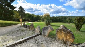 Ein Kiesweg führt durch einen Park mit großen Steinen, einer hölzernen Bank und blauem Himmel.