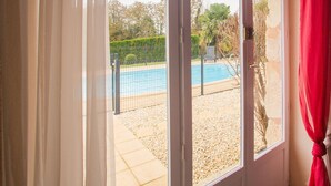 Blick durch ein Fenster auf einen Pool, eine Terrasse mit trittsteinartigen Elementen und einen roten Vorhang auf der rechten Seite.