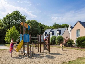 Ein Spielplatz mit Klettergerüsten und einer Rutsche, umgeben von Kieswegen und Wohnhäusern.