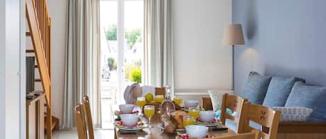 A dining area with a wooden table set for breakfast, chairs, a hanging light fixture, and a view of the outdoors through a glass door.