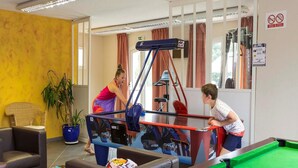 Uma sala de jogos com mesa de sinuca, uma área de estar com sofá e poltronas, e equipamentos de ginástica.