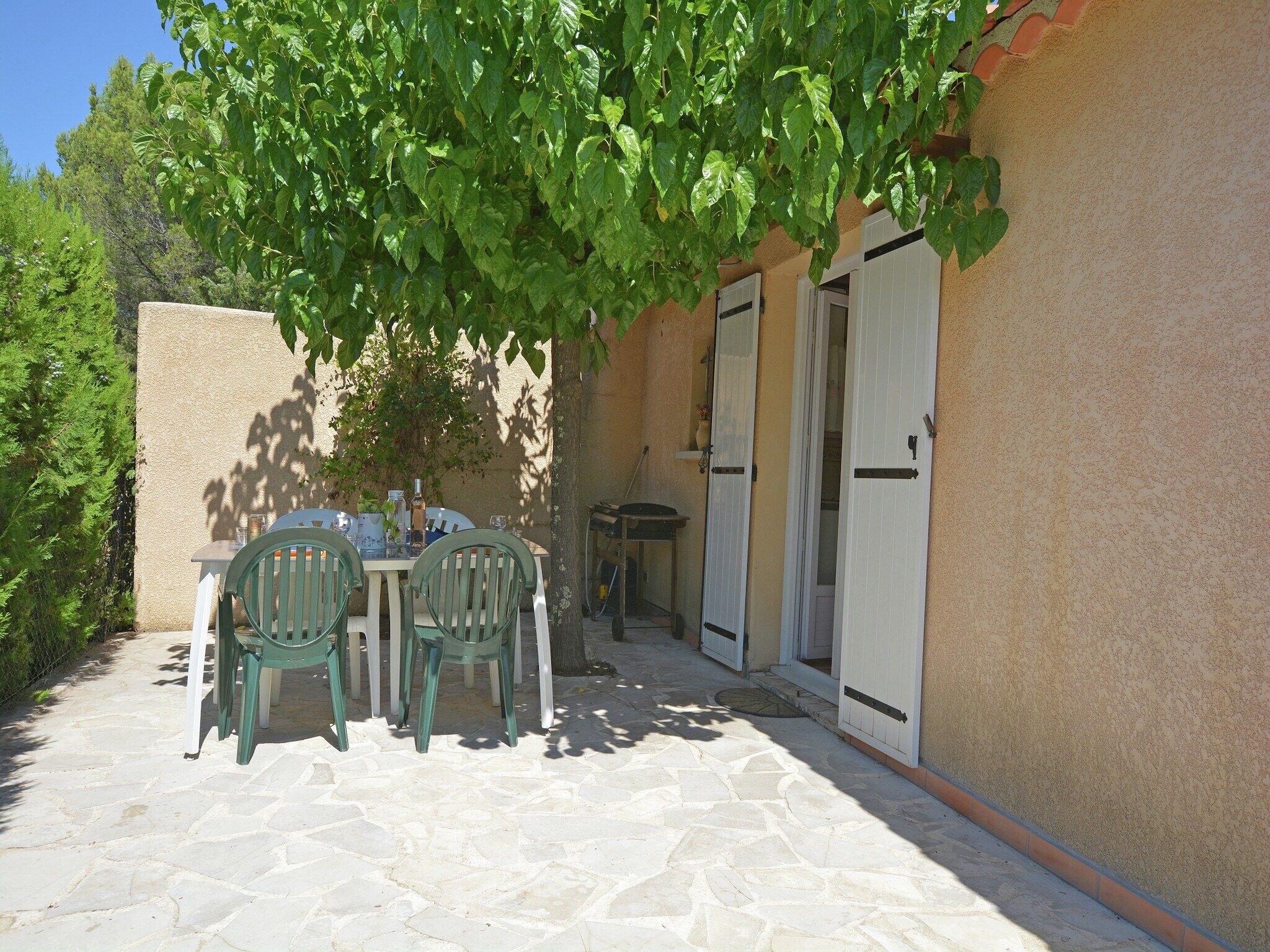 An outdoor patio with stone flooring, a table, two chairs, and a door.