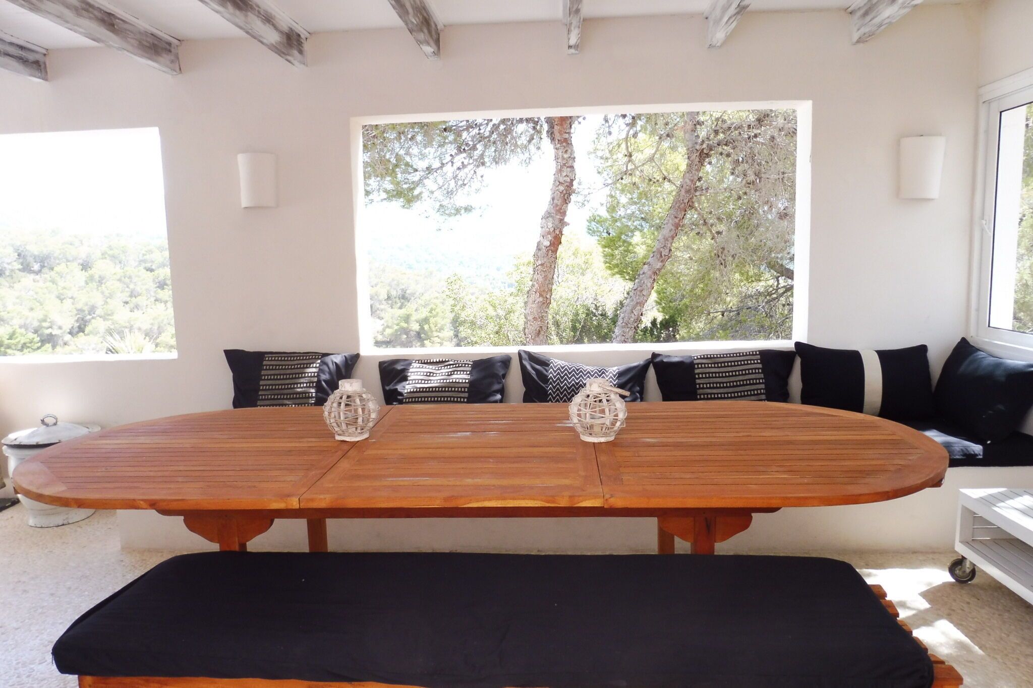 Une table de salle à manger en bois, agrémentée de coussins noirs, d’un banc et de deux lanternes décoratives.