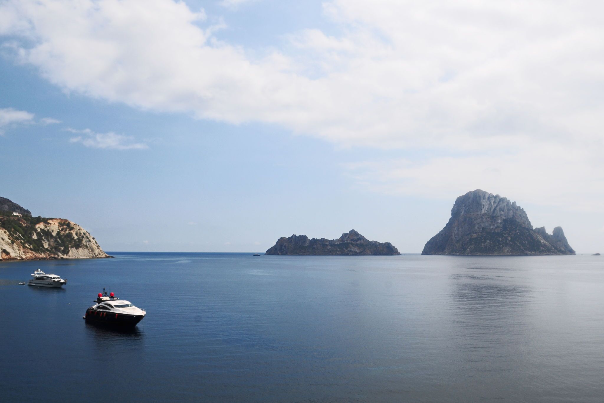 A calm sea with boats and a large rock formation in the distance.
