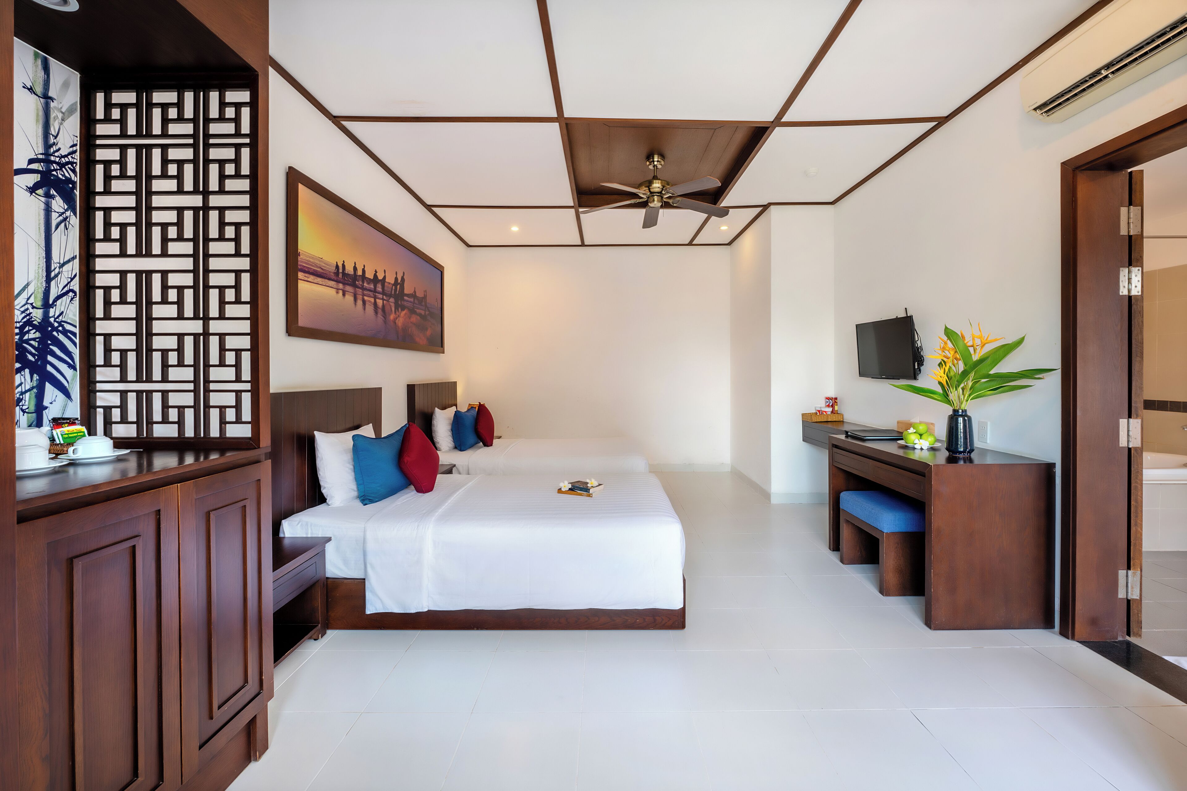 A hotel room with a large bed, a desk, a TV, and a ceiling fan.