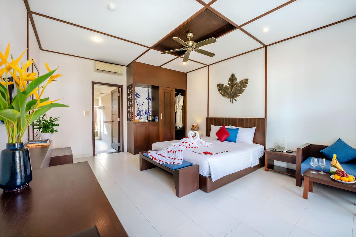 A modern hotel room with a large bed, a seating area with a table, and a ceiling fan.