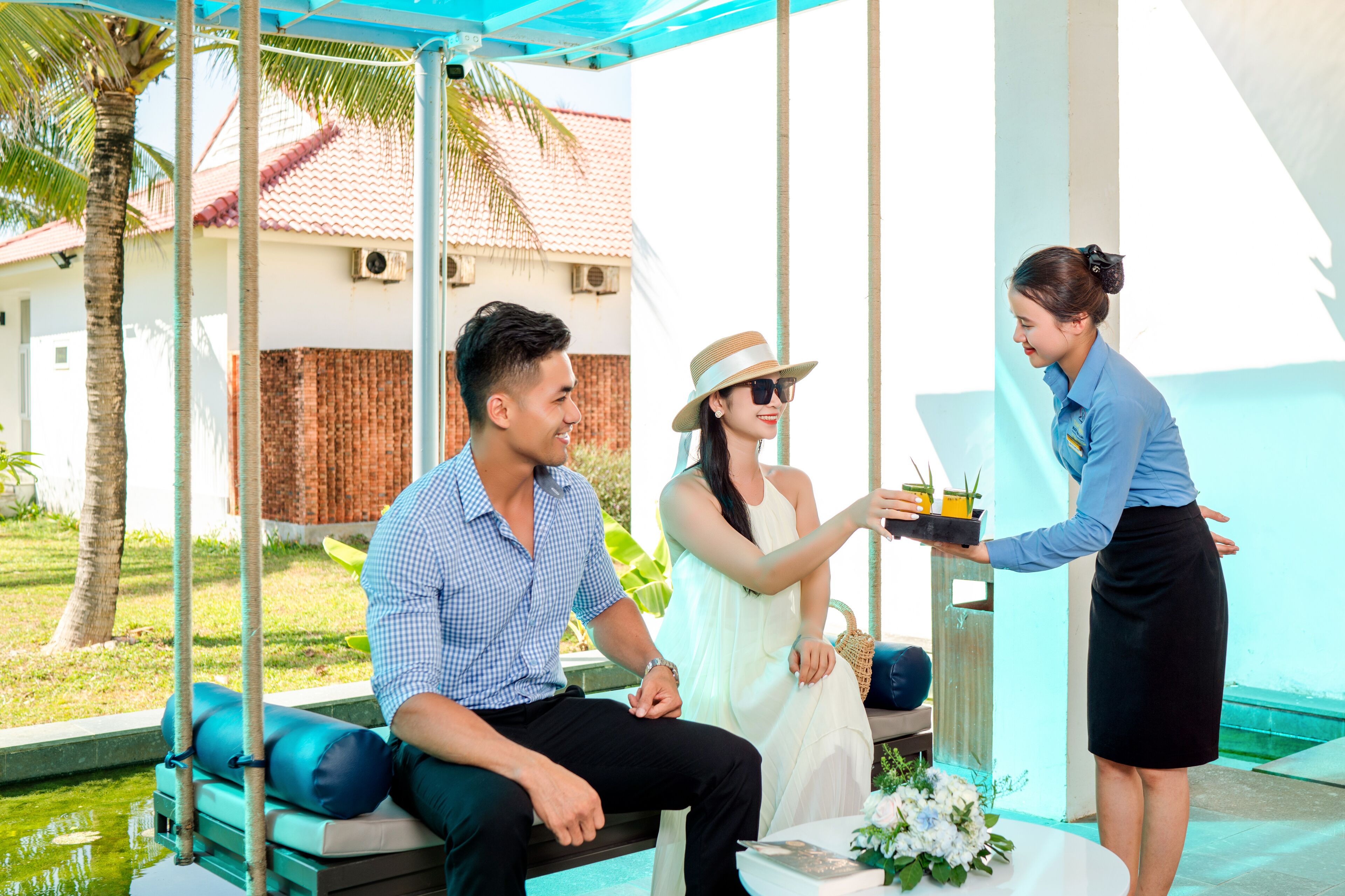 A couple seated on a swing with a pool and palm trees in the background.