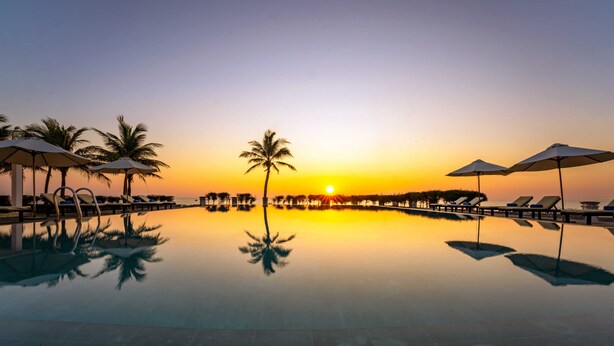 Vista al lado de la piscina al atardecer, con sillones y sombrillas.