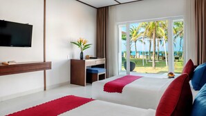 Una habitación de hotel con dos camas, un escritorio, un televisor y vista a la playa.