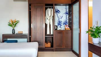 A hotel room with a bed, a desk with a vase of flowers, a wardrobe, and a sliding door with a plant on the right.