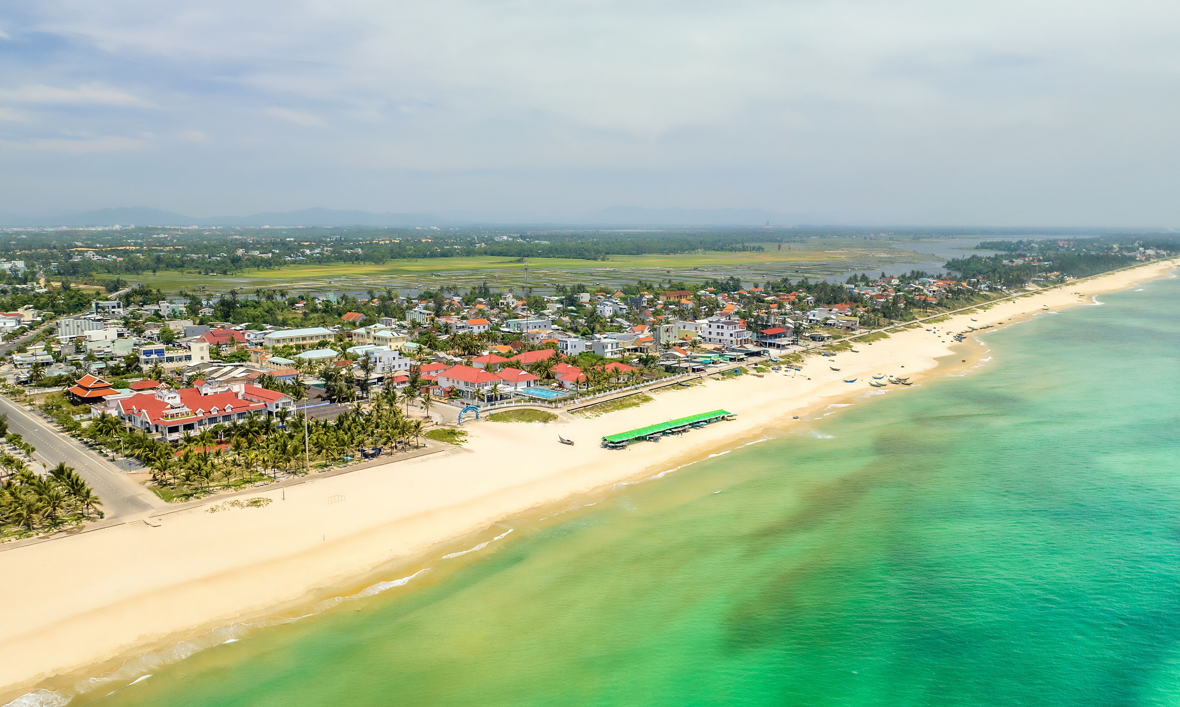 An aerial view of a coastal town with a beach, houses, and a road.