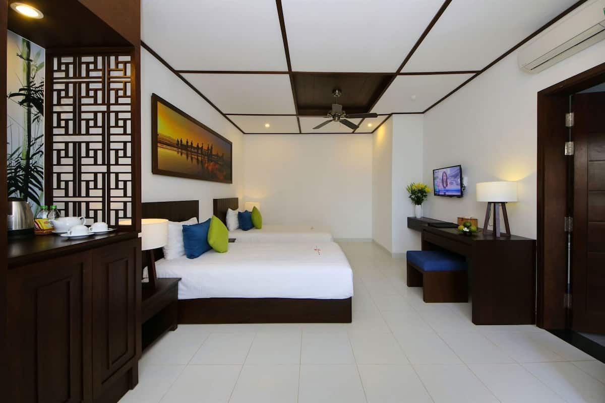 A hotel room with two beds, a desk with a computer, a TV, and a decorative screen.